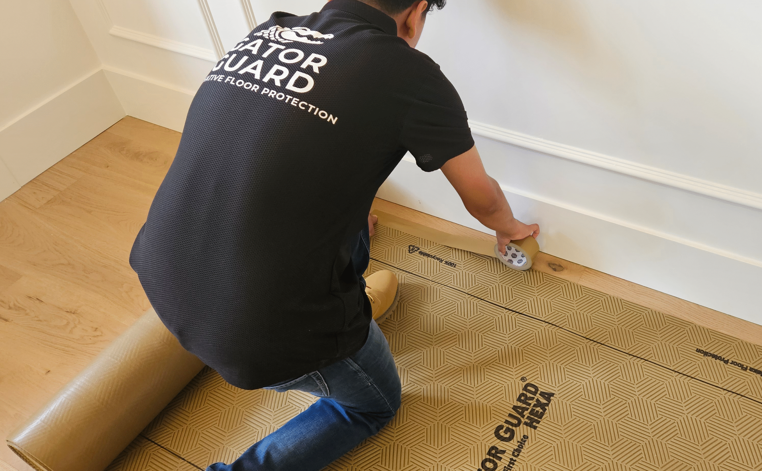 Worker installing Gator Guard Gold protective floor covering during construction. Durable, reusable, and easy-to-install surface protection for hardwood floors.